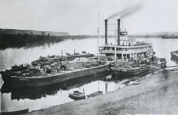 View down hill towards "Diamond Jo" steamboat docked on the shoreline of the Mississippi River while goods are being loaded onto the steamboat.
