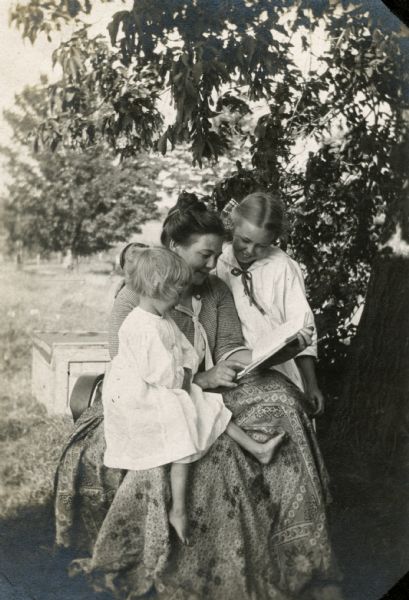A mother reads to her two children outdoors.
