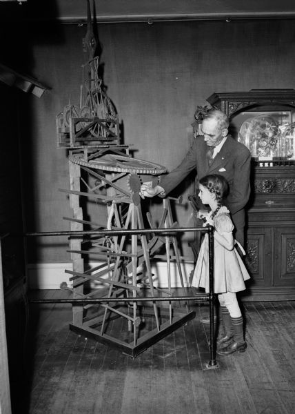 Photograph of clock made by John Muir while a student at the University of Wisconsin in 1860. A young girl, and Charles Brown of the Wisconsin Historical Society staff, look at the John Muir clock on display at the State Historical Society of Wisconsin. John Muir (1838-1914) was America's most famous and influential naturalist and conservationist. He is one of California's most important historical personalities. He has been called "The Father of our National Parks," "Wilderness Prophet," and "Citizen of the Universe."