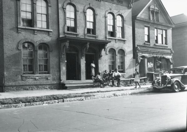 Group of People in front of Building Group of people on steps in front of unknown building in Milwaukee. A car is parked on the street.