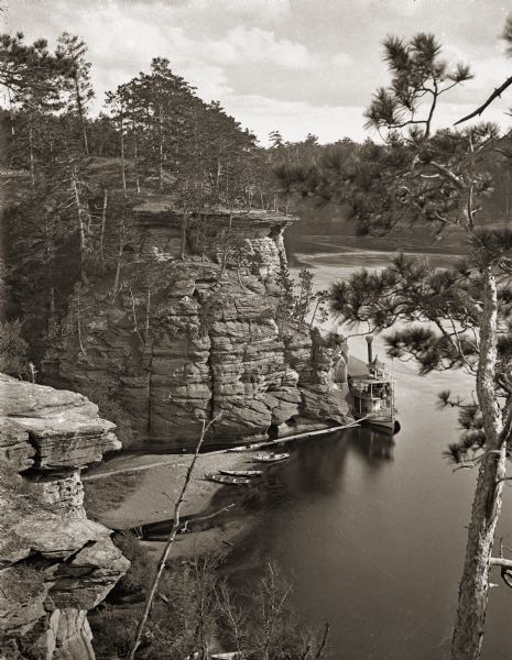 Mouth of Witches' Gulch and downstream, viewed from cliff. Steamboat <i>Alexander Mitchell</i> at mouth of gulch. Four canoes are on shore.