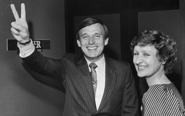 Governor Martin Schreiber displays the V for victory sign as his wife stands with him, smiling.
