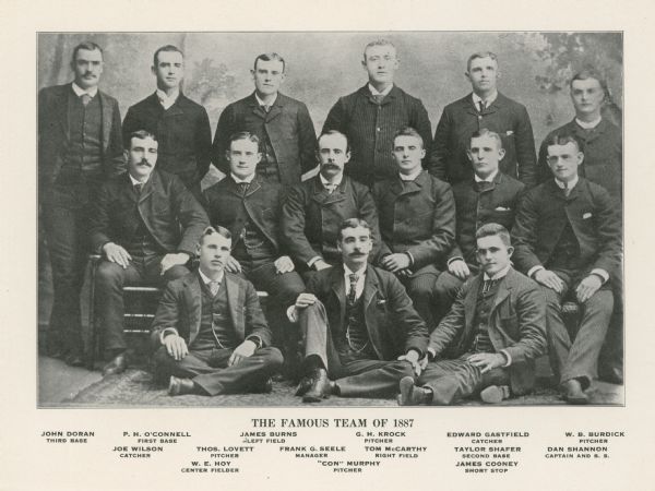 A studio group portrait of the Oshkosh baseball team, "The Famous Team of 1887". All the players are wearing formal suits rather than baseball uniforms. In the front row, seated left to right on the floor, are: W.E. Hoy (center fielder), "Con" Murphy (pitcher), and James Cooney (short stop). In the middle row, seated left to right on chairs, are: Joe Wilson (catcher), Thomas Lovett (pitcher), Frank G. Seele (manager), Tom McCarthy (right field), Taylor Shafer (second base), and Dan Shannon (captain and short stop). Standing left to right in the back row are: John Doran (third base), P.H. O'Connell (first base), James Burns (left field), G.H. Crock (pitcher), Edward Gastfield (catcher), and W.B. Burdick (pitcher).