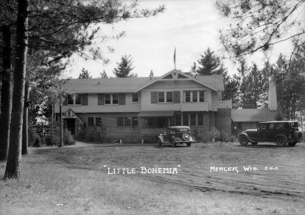 Exterior view of Little Bohemia Restaurant and Lodge with multiple vehicles parked out front.