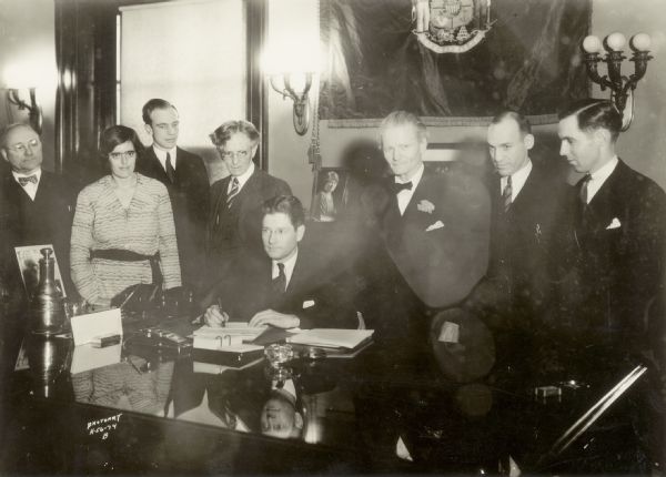 Governor Philip La Follette signing Wisconsin's pioneer unemployment compensation law. From left to right are Henry Ohl, Elizabeth Brandeis, Paul A. Raushenbush, John R. Commons, Governor La Follette, Henry A. Huber, Harold M. Groves, and Robert A. Nixon.