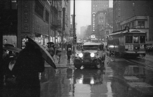 Automobile traffic, with a street railroad car in the background, on a rainy day.