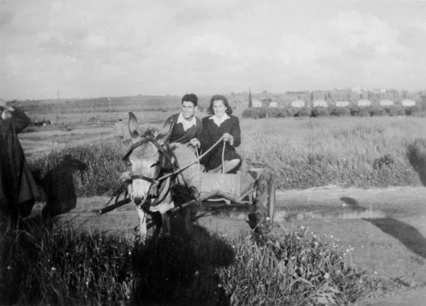 Susanne Hafner Goldfarb and unidentified friend ride in a cart pulled by a mule; Raanana, Israel.