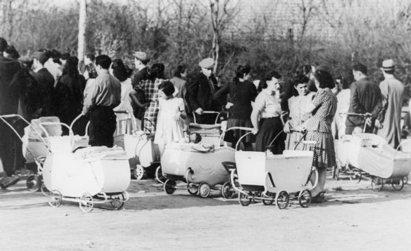 A group of unidentified refugees are standing near baby carriages at a Displaced Persons camp in Germany.

