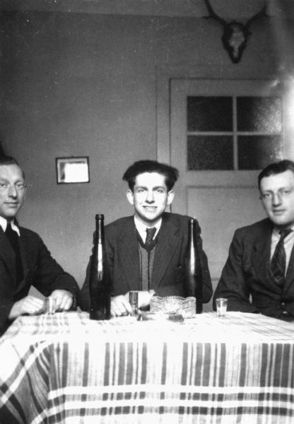 Group portrait of Holocaust survivor Fred Platner (left) seated at a table with his cousin, Heini Petzenbaum (center), and his brother, Isidor (right); Hannover, Germany.