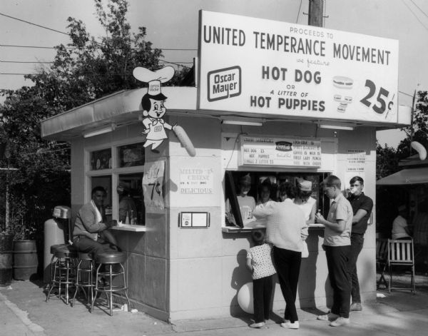 Fundraising booth of the United Temperance Movement of Wisconsin at the Wisconsin State Fair.  At that booth one could purchase soft drinks, milk, and "first lady punch" that supported the organization's statewide public education program.  The booth also sold Oscar Mayer brand hot dogs and "hot puppies" and displayed the Little Oscar sign.