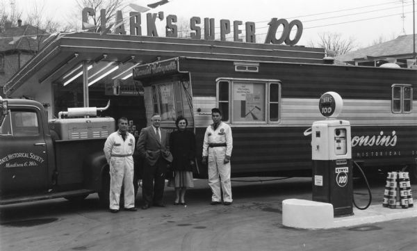 The State Historical Society of Wisconsin's Historymobile at the Clark Service Station, 2631 University Avenue. Mr. and Mrs. J.J. Tschudy (Jake and Irene), Curators of the Historymobile, center, were greeted by Dick Casper, right, manager of the station, and Jack Spahr, the attendant at left.