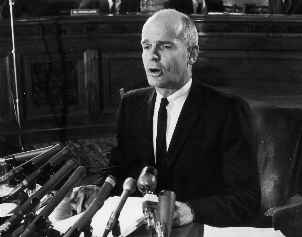 Senator William Proxmire giving a speech in front of several microphones.