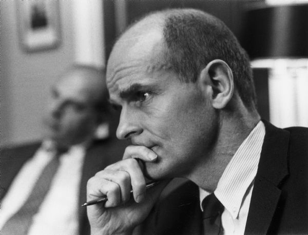 Close-up of Senator William Proxmire listening pensively while holding a pen in his hand.