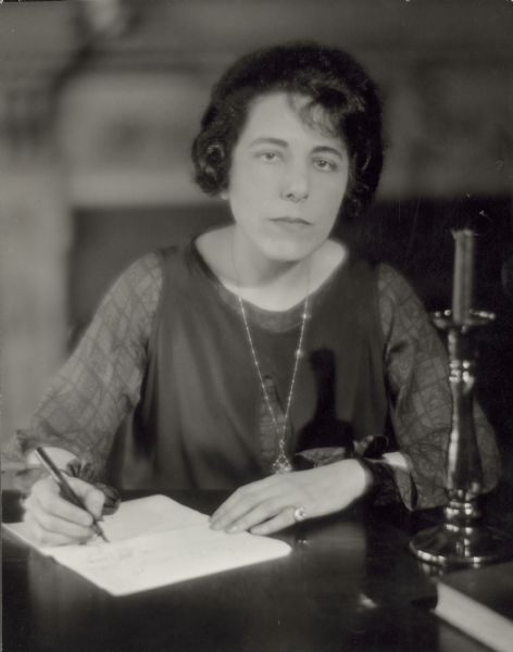 Portrait of Edna Ferber seated and writing with a pen.