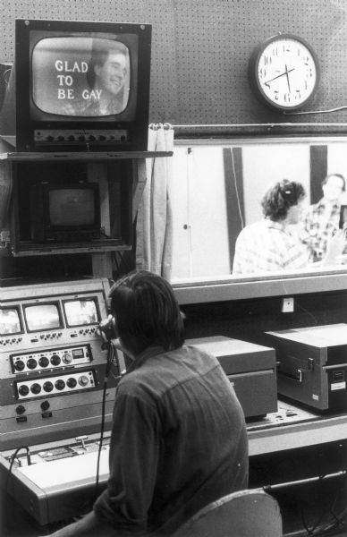 Michael Henry is seated at the mixing board at a local television station. There is a cable access program playing on the monitor above him called "Glad To Be Gay."