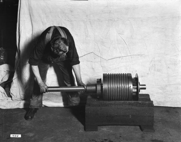 Man assembling a load-brake ratch on a type "A" trolley, possibly at the Pawling and Henry plant. The man is leaning over, and behind him is a drop cloth.