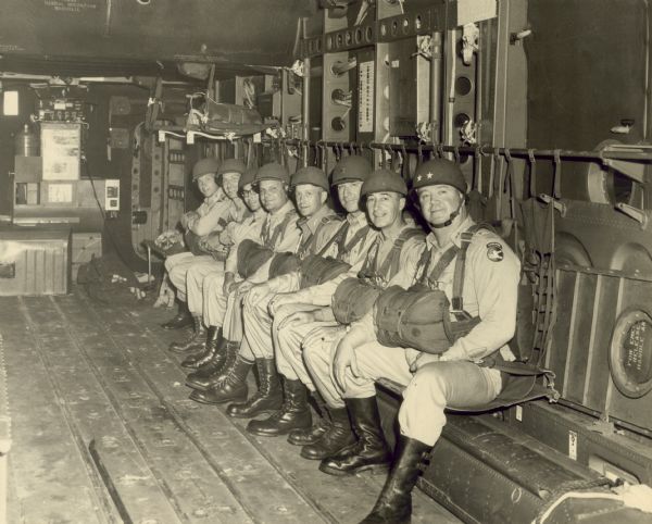 Paratroopers of the 82nd Airbourne division seated in a C-82 prior to takeoff. From right to left are Major General Ralph M. Immell (commander of the 84th Airbourne division), Colonel Edward L. Carmichael, Colonel Harold W. Gardener, Colonel Austin T. Thorson, Colonel Leslie V. Dix, Captain Clarence A. Schoenfeld, Major Patrick W. Cottber, and Major Gregory R. Endre.