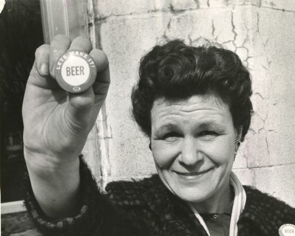 Close-up of Mrs. Edna Ann Vistart holding up a button bearing the slogan: "Beer, Let's Make It!"