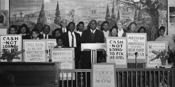A New Orleans group hold signs as they rally at Mercy Seat Baptist Church for compensation for lives lost and 25,000 homes ruined during a flood. Reverend Roosevelt Johnson stands in the center of the group. Walter and Elizabeth Rogers, also flood victims, stand in the back row.