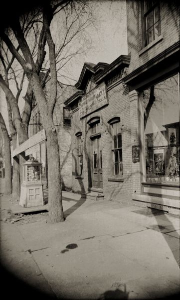 Exterior view of the H.H. Bennett Studio storefront, in Kilbourn (former name of the Wisconsin Dells). A display case of Bennett's images is on the wooden sidewalk in front of the store.