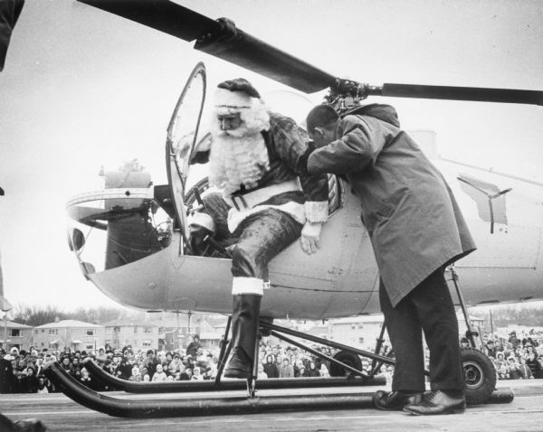 As a crowd of onlookers watch, Santa Claus alights from his special holiday helicopter with the help of an aide at Southgate Shopping Center.