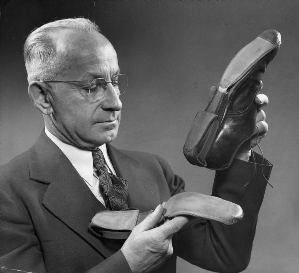 A man, possibly inventor Leo Kay, holding a slipover bowling shoe, which attaches to a regular street shoe.