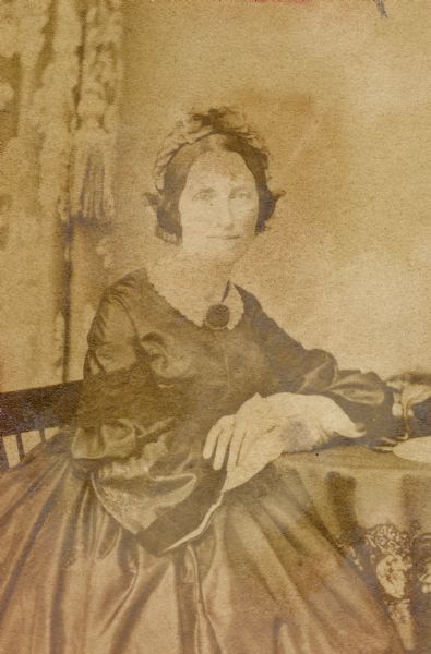 Studio portrait of Catharine Eaton. She is wearing a dress and is seated in a chair with her arm resting on a table.