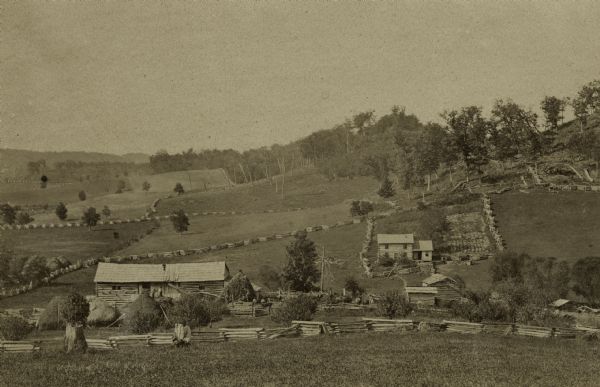 View from a distance of a farm in a valley owned by Alex(ander?) Smith. There is a wooden fence in the foreground surrounding the farm.