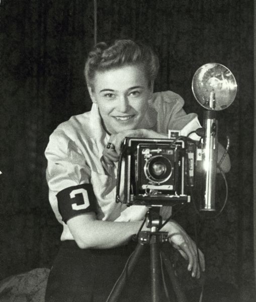 Dickey Chapelle wearing correspondent armband and taking a self-portrait in mirror. Taken at time of her first recognition by War Department as "Look's" photographer.