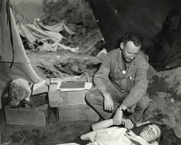 Lt. Commander Leonard (Leo) Thelen, Commanding Officer of the hospital, taking the pulse of a Marine line officer whose legs have been injured by shrapnel.
