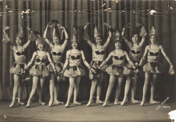 Eight young dancers in costume pose onstage.