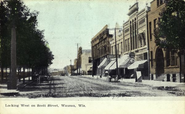 View of Scott Street, looking westward. A horse-drawn carriage is parked near a large sign for a drugstore. Caption reads: "Looking West on Scott Street, Wausau, Wis."