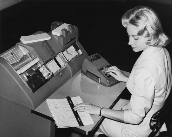 A student studies key punch operation in a data processing class at Milwaukee Vocational and Adult Schools. She is seated at a very large computer.