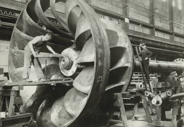 Men work on a huge, metal water wheel at Allis-Chalmers Manufacturing Company.
