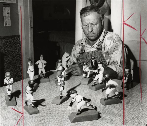 Walter Lofblad, a Cumberland farmer, with miniature Milwaukee Braves figures he carved from basswood. The carved set includes the entire starting lineup, manager Charlie Dressen, an umpire, and a spectator. Lofblad also holds a carving of a bear.