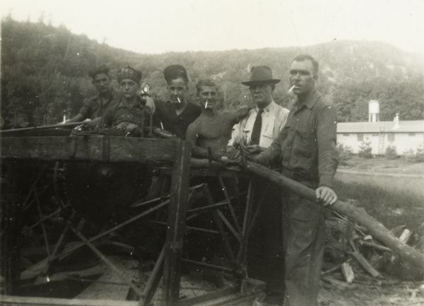 Group of Civilian Conservation Corps workers standing at a table saw. One man, probably a supervisor, wears a hat and tie.