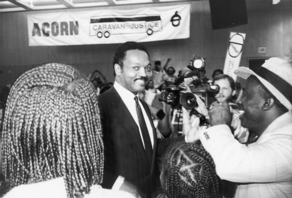 Jesse Jackson stands beneath an ACORN banner as he is photographed by a crowd of people.