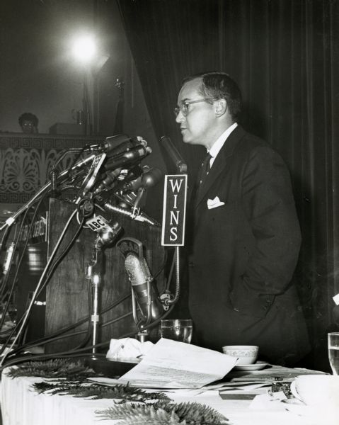 Newton Minow Making a Speech Newton Minow stands before many microphones making a public speech.