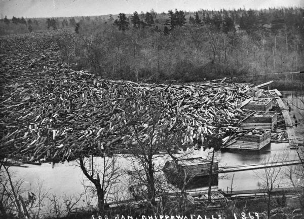 Elevated view from steep shoreline of a log jam of about 150 million feet of logs, stopped at the piers of Pound, Halbert, and Co., which stood in about 40 feet of water. In some places the logs piled up 20 feet above the water.