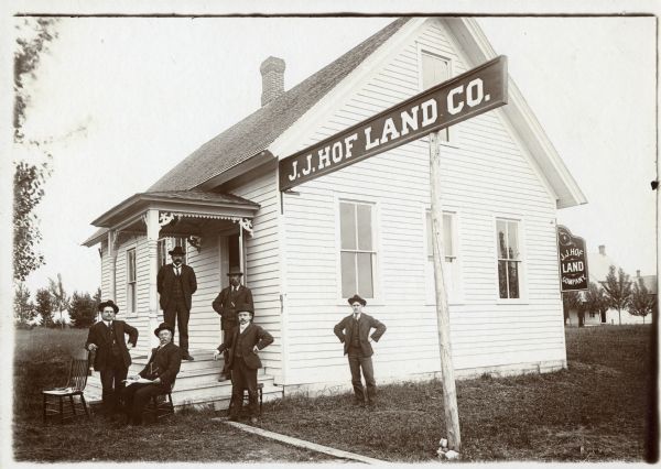 Six men in suits and hats, probably employees of J.J. Hof Land Co., in front of the company office building.