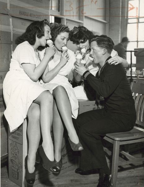 Sailor and Women with Ice Cream Cones Three women in white dresses sit on a box nest to a young sailor sitting on a chair. They are all eating ice cream cones.