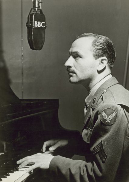 Marc Blitzstein in U.S. Army Air Corps uniform at a piano, singing into a BBC microphone. Caption on reverse of image reads "London, 1943".
