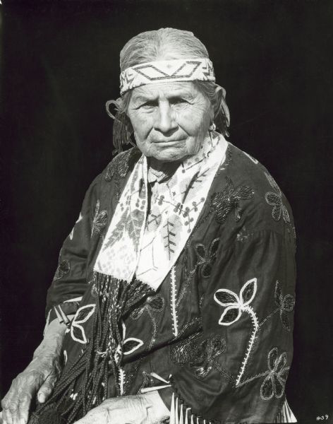 Portrait of Menoninee Indian performer in full dress seated for waist-up portrait. Member of the Peavey Falls group of dancers and musicians from the Menominee Indian Reservation in Wisconsin.