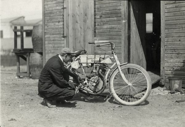 A man crouches down for a close look at a 1905 model Harley-Davidson motorcycle.