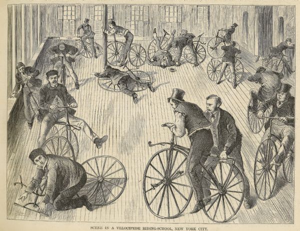 Engraved image of several men attempting to ride velocipedes in a large open, interior space. Many have fallen or are struggling with balance.