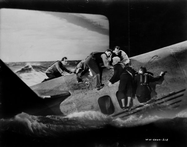 Scene still of people crawling out of and on an airplane in the water from the film "Foreign Correspondent." In the background is a rear projection screen showing rough seas.