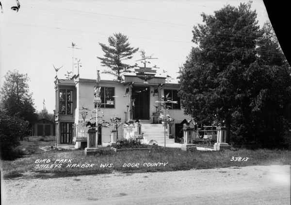 House built by Albert Zahn, Sr. He carved figures of angels, animals, and birds, and after his wife painted them, he mounted them on pillars in the yard. A dog is lying in the yard near the foundation of the house on the left.