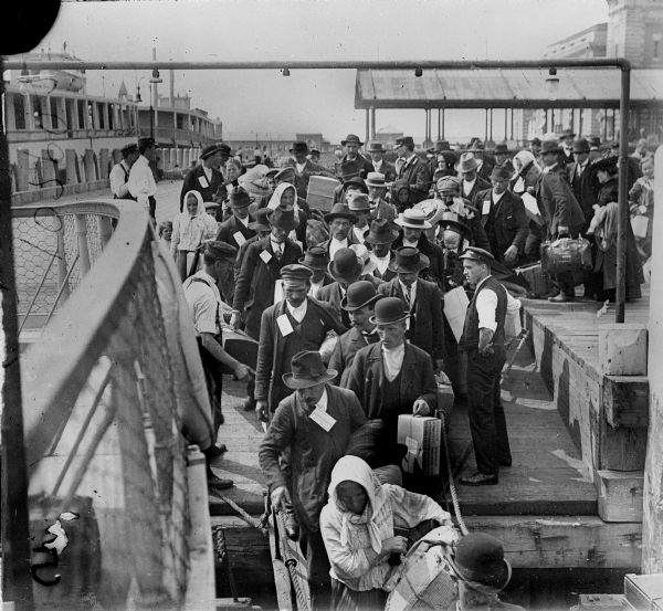 Elevated view from railing of immigrants boarding a ferry to depart Ellis Island.