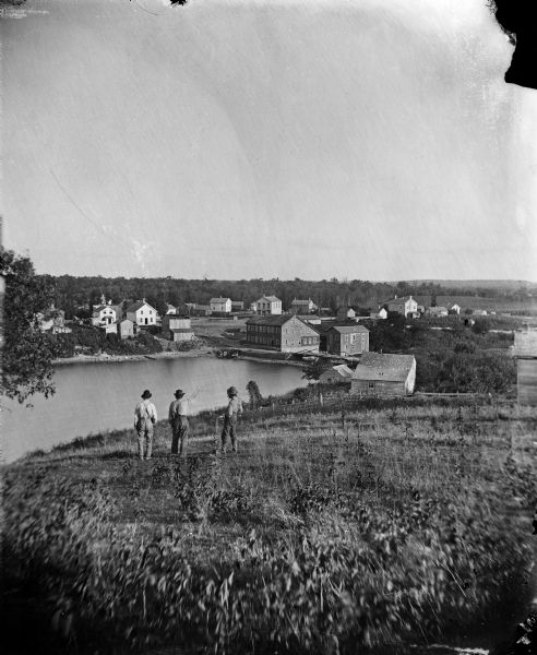 Elevated view from hill of Clinton, now Rockdale. Three men are in the middle distance, looking east across Koshonong Creek towards a mill dam, bridge and carding mill.