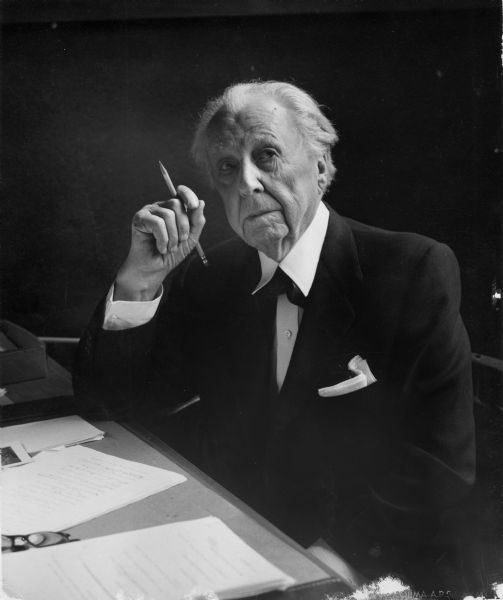 Portrait of Frank Lloyd Wright seated at a desk.